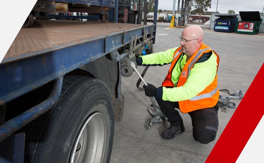 A man in high visibility gear fixes a strop to a truck.